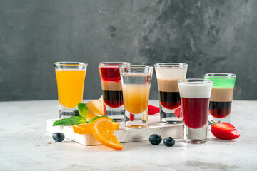 Various alcoholic drinks in glasses on a white table, mixed shots of berries and oranges
