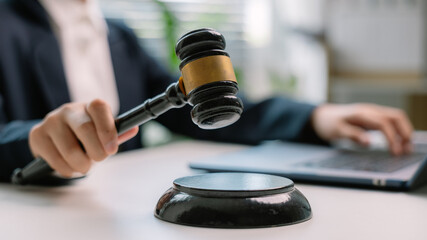 Close-up of judge's hand holding gavel with laptop in background, representing legal decision, online courtroom, law and justice, digital legal services, and modern judicial system.