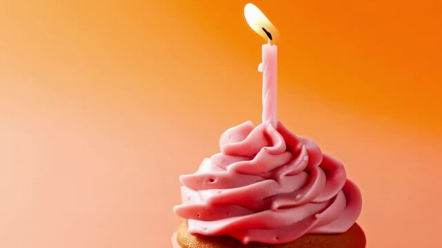 Cupcake with pink frosting and a lit candle on an orange background, birthday celebration