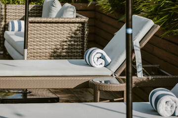 A lounge chair with a soft cushion and a blue and white rolled up towel surrounded by lush greenery outdoor at daytime along the pool of a hotel in Manila during a summer holiday in the Philippines.