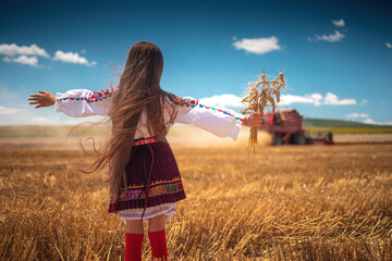 Young girl with traditional Bulgarian folklore costume at the agricultural wheat field during harvest time with industrial combine machine