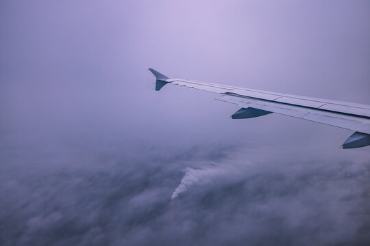 Airplane flying over color sky clouds during scenic sunset or sunrise cloudscape, view from plane window of wing turbines and horizon