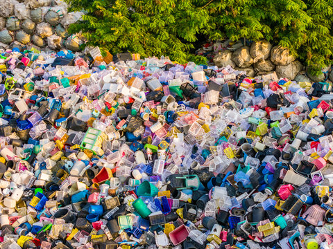 Pile of colorful household waste and discarded containers near green tree