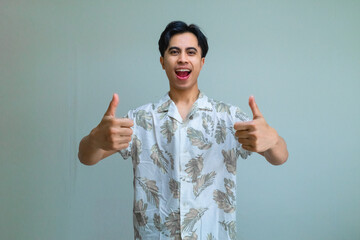 Happy young Asian man in summer clothes smiling and giving two thumbs up to the camera, expressing excitement and positivity, isolated on a clear background