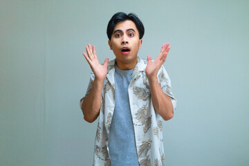 Portrait of a young Asian man in summer clothes with a shocked facial expression, looking directly at the camera against a clear background, perfect for surprise or reaction concepts