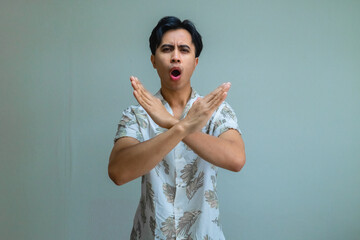 Portrait of a serious young Asian man in summer clothes making a stop gesture with his hand, isolated on a clear background, expressing warning or refusal