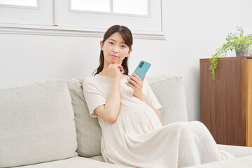 スマートフォンを持って考える妊婦　リビング