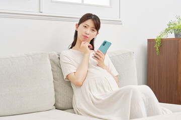 スマートフォンを持って考える妊婦　リビング