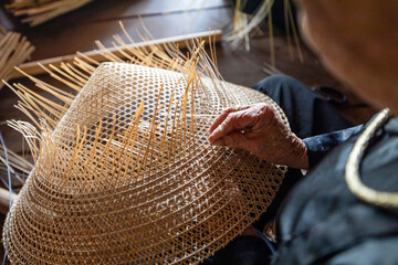 Close-up of artisan's hands weaving palm leaves to make traditional conical hats (Non La) in a craft village at ATK Dinh Hoa historical site.