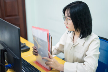 Young Asian woman reviewing documents at her workstation during office hours in a modern workspace