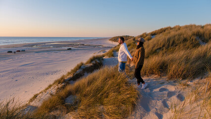 Two couples stand hand in hand on a dune overlooking the tranquil beach in Denmark during a stunning sunset. The golden hour light illuminates the serene landscape, Vejers Strand beach Denmark