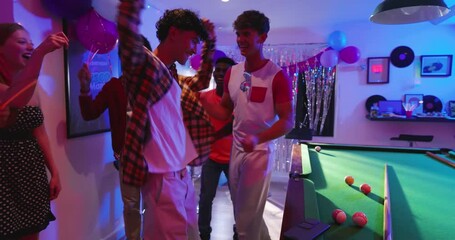 Diverse friends dancing around pool table in game room under disco ball as music plays - Powered by Adobe