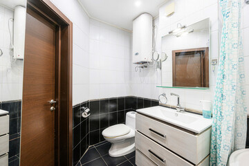 bathroom with black and white tiles features a toilet, sink, mirror, water heater, and brown door. A patterned shower curtain is visible