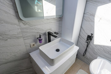 white sink, black faucet, and soap dispenser against marble-like tile. Clean design with minimalist aesthetics