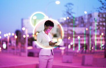 Businesswoman using smart phone while standing near illuminated icon and graph in city