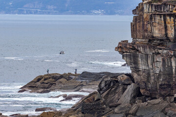 Fishermen on the shore below the sandstone cliffs in the Royal National Park, Sydney Australia