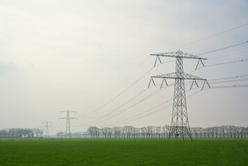 Power lines in a green field during spring with a cloudy sky