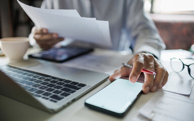 asian businessman using mobile phone and laptop working reviewing document and business contract on desk in office