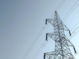 High voltage power lines on towering steel pylons transmit electrical energy across the blue sky © Afrizal Oficiall