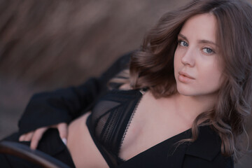 Naklejka premium A female model poses sitting on a chair among nature and fields, an unusual photo of a summer Look