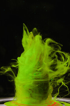 Vibrant yellow and green ink creates tornado shapes in water against a black background
