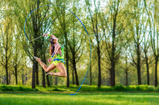 Young woman performing rhythmic gymnastics with ribbon in a green meadow outdoors