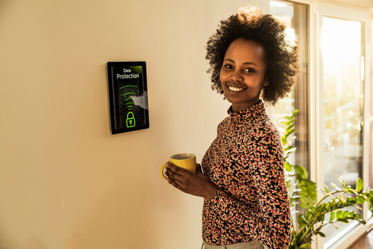 Smiling woman with coffee cup standing by home automation device