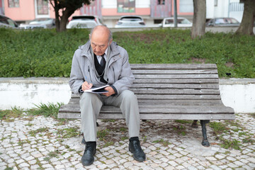 Obraz premium Senior professor writing notes outdoors on park bench