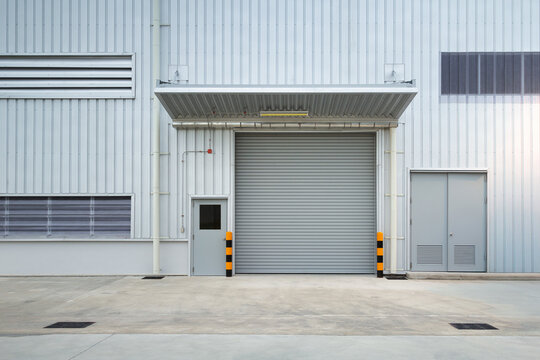 Exterior of industrial building. Construction for factory, store or warehouse. Include shutter door at front. Nobody empty space on concrete floor suit for product display or industrial background.