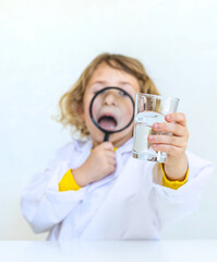 A child examines water with a magnifying glass. Selective focus.