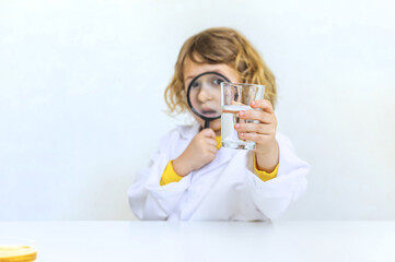 A child examines water with a magnifying glass. Selective focus.