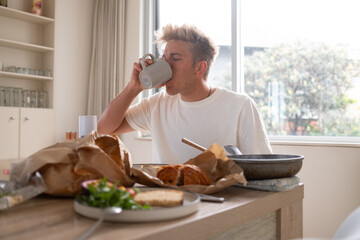 oung man drinking coffee while having breakfast at home