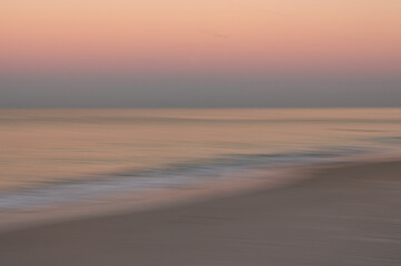Smooth abstract ocean water waves under pink, blue, pastel sky