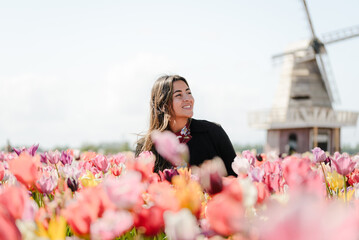 Fototapeta premium Woman Smiling in Front of Traditional Dutch Windmill and Tulips