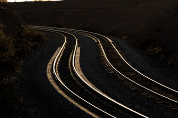 Parallel curved railroad tracks glint in the last light