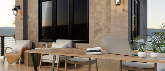 Laptop on wooden table with books and potted plants at balcony or terrace of a brown painted house.