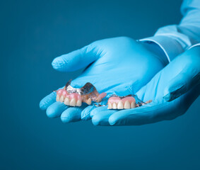The dentist is holding dentures in his hand against a blue background