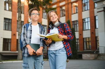 Positive schoolchildren preparing schoolwork, sitting on steps outside school in sunny autumn day