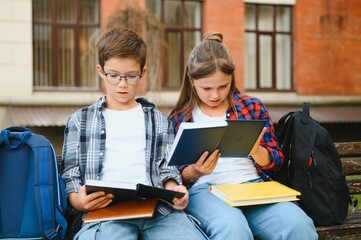 Group of elementary school children reading books having an outdoor class of modern school building...