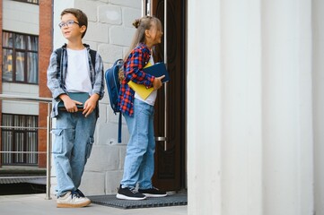 two younger students with backpacks approach the entrance to the school of red brick, the concept...