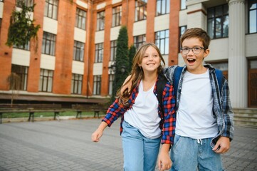 Happy school kids friends boy and girl with backpacks walking and laughing having fun together near school building outside outdoor after lessons