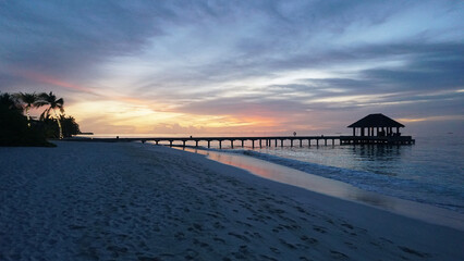 Stunning sunset illuminating the indian ocean, featuring a picturesque jetty and swaying palm trees on a maldivian beach, creating a serene and tranquil atmosphere perfect for relaxation