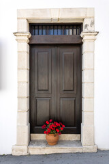 Brown wooden front door in white stone doorway and potted red flowers, Cyprus