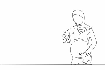 Single one line drawing small shoes for unborn baby in belly of pregnant woman. Arabian pregnant woman holding small baby shoes relaxing at home in bedroom. Continuous line draw design graphic vector