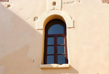 Narrow vertical arched window set into smooth light-colored wall