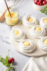 Meringues mini pavlova cakes with lemon cream served on a tray on white marble background. Light summer dessert