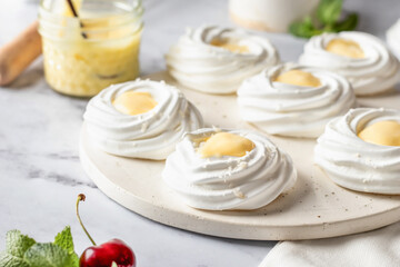 Meringues mini pavlova cakes with lemon cream served on a tray on white marble background. Light summer dessert