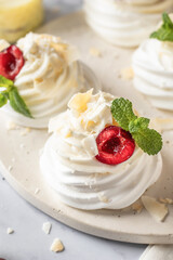 Meringues mini pavlova cakes with whipped cream decorated with fresh cherry berries and mint leaves close up. Light summer dessert