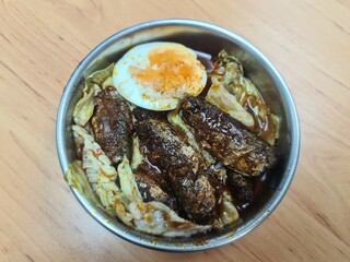 Fried mackerel fish with spicy sauce served with boiled egg and boiled vegetables in a stainless steel bowl on wooden table