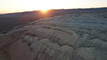 The sun sets behind a mountain range, casting a warm glow over the eroded desert landscape, creating a breathtaking view of nature's artistry